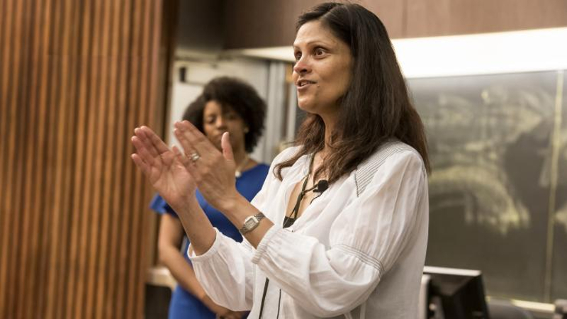 Nimmi Ramanujam in a white lab coat giving a talk during an event