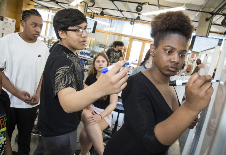 Students write on boards during the hackathon held at the Design Pod at Duke University in March 2023.