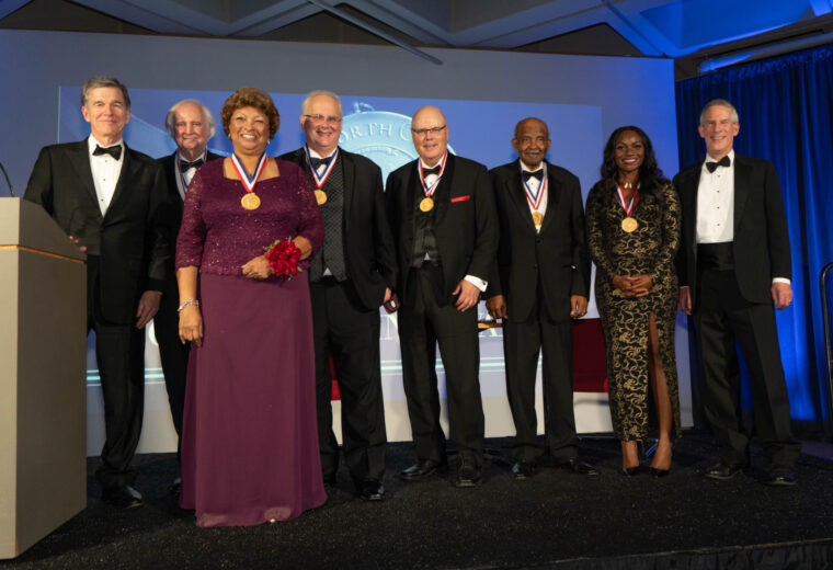 eight people in evening attire and wearing medals around the necks stand abreast