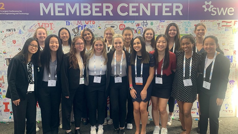 A group of female Duke engineering students pose together in front of a conference sign